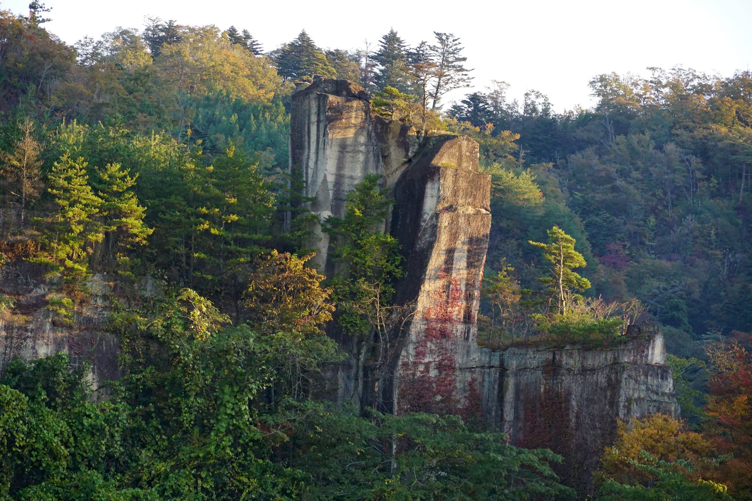 A tall weathered rock pillar among autumn trees on the valley side at Akiu Onsen