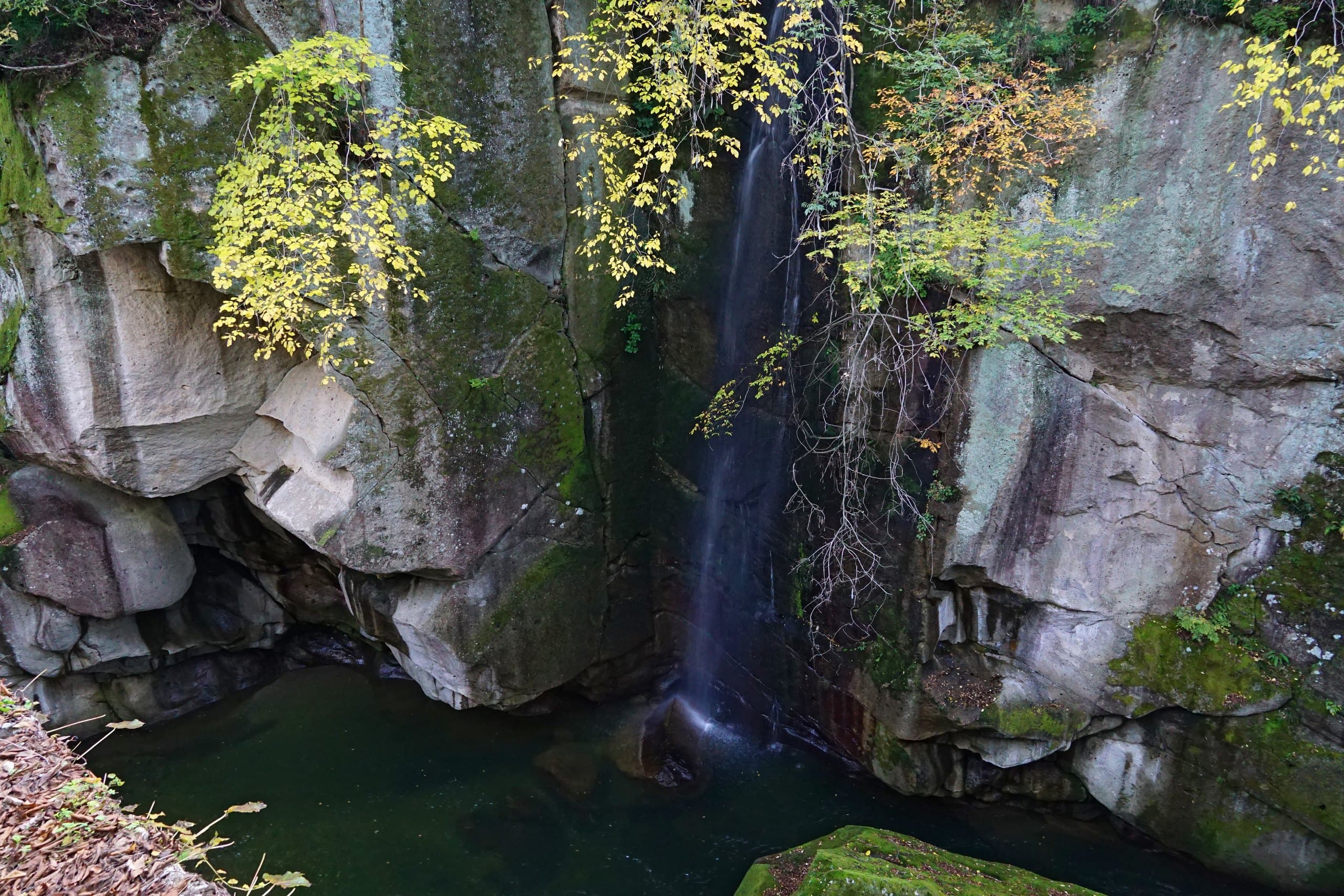 A thin waterfall dropping into a pool between rock walls in Rairaikyo gorge