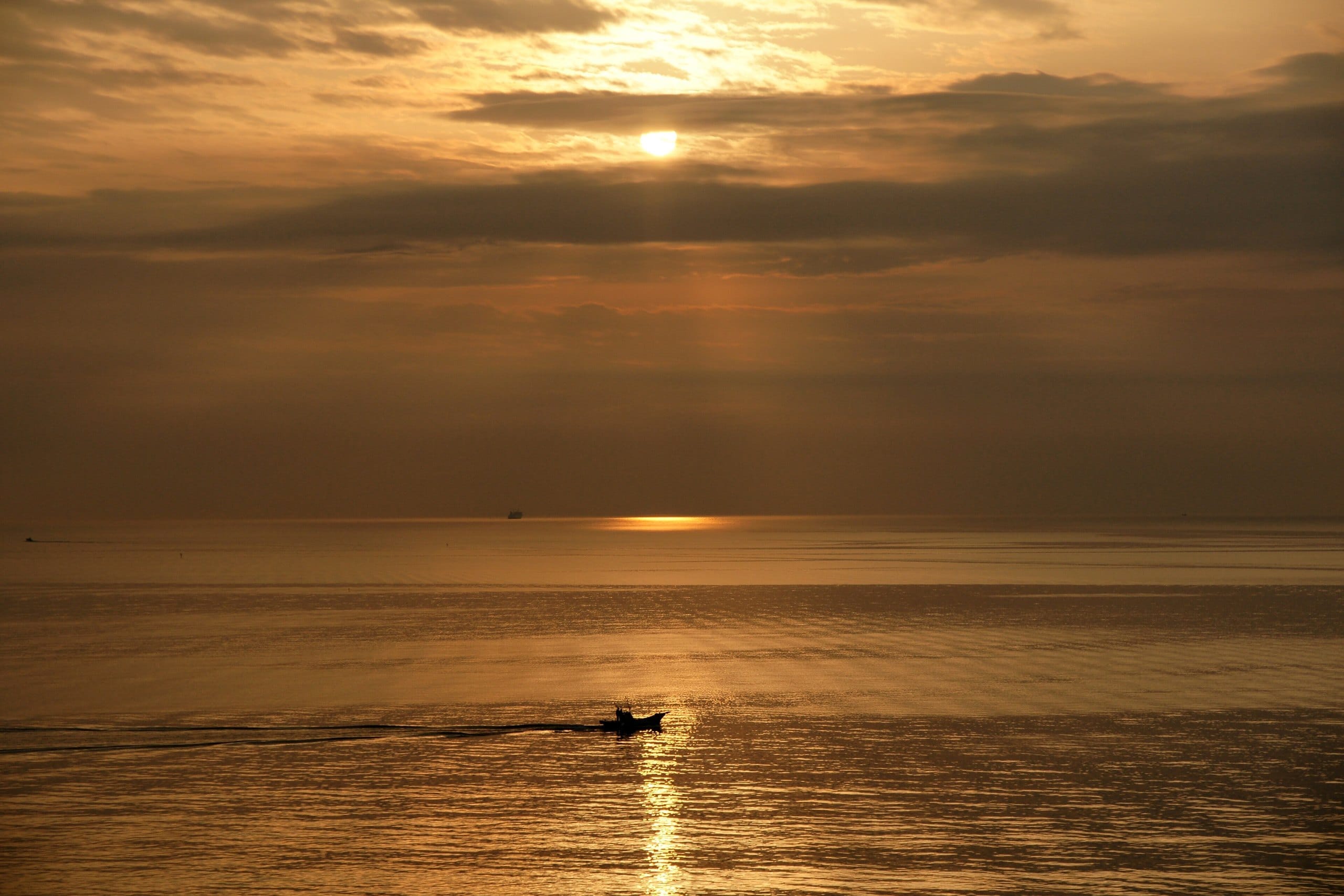 Morning sun glowing over Beppu Bay with a small boat on golden water