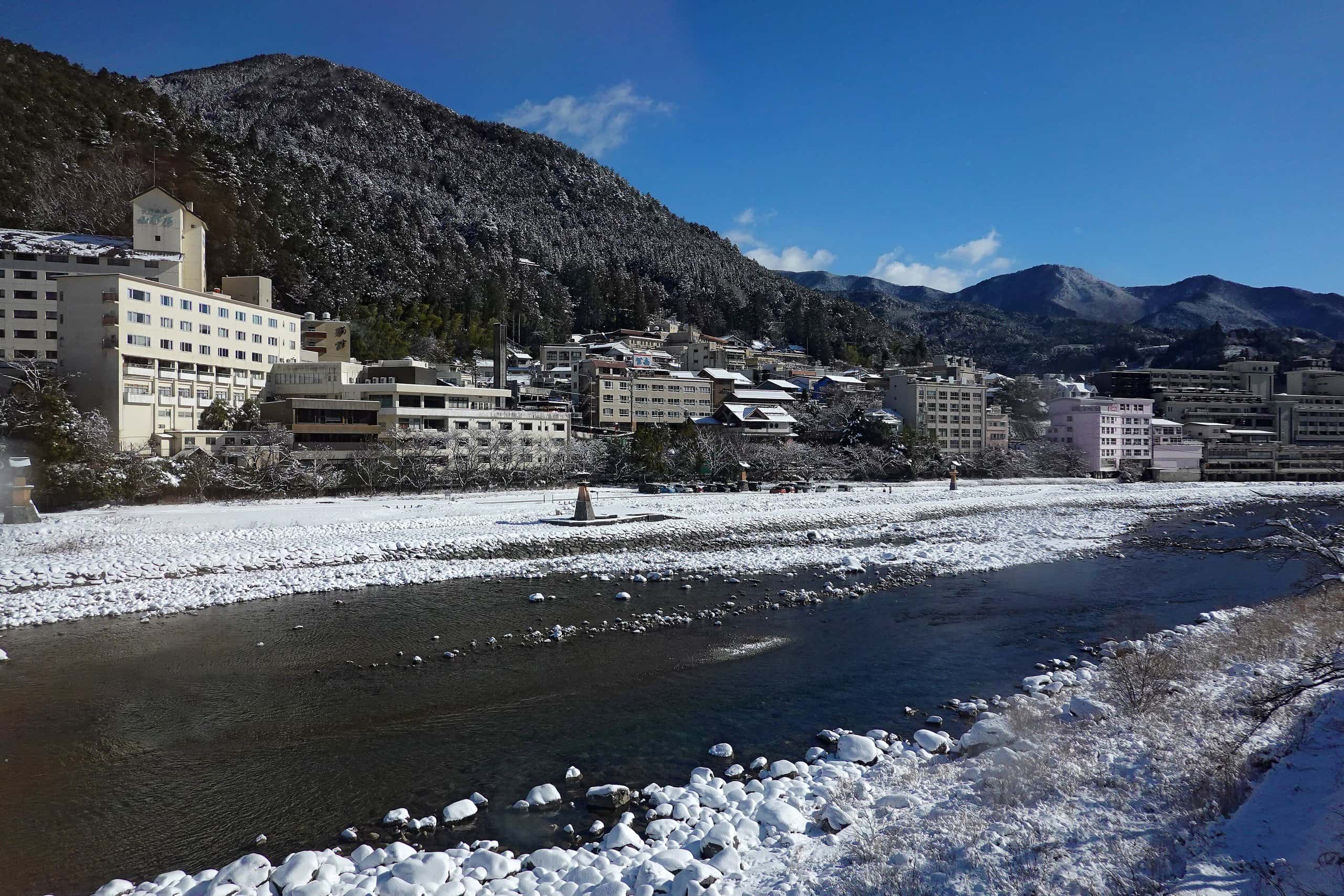 Snow-dusted riverbed of the Hida River with Gero's onsen town and wooded hills behind