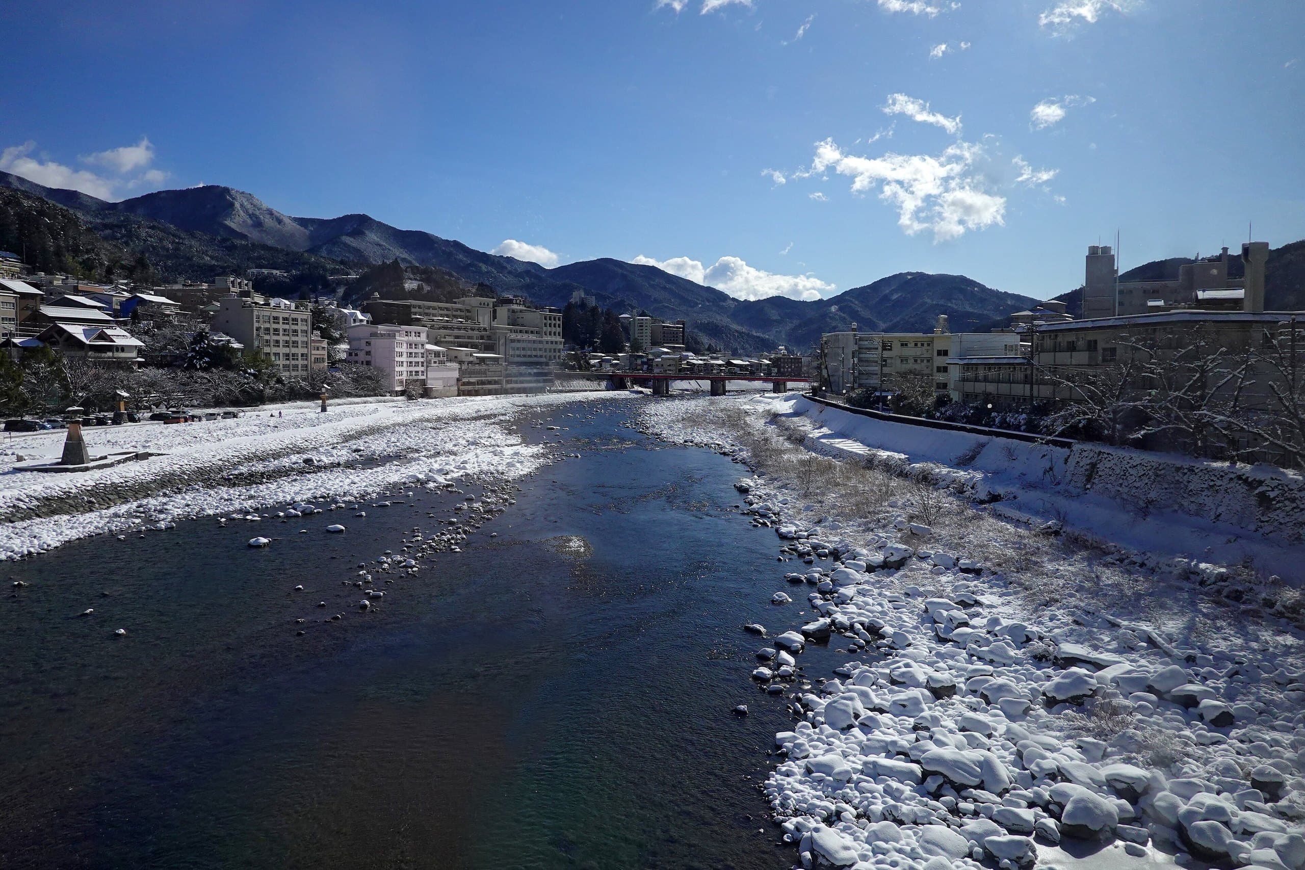 Clear Hida River flowing between snowy banks toward the Gero onsen town and distant mountains