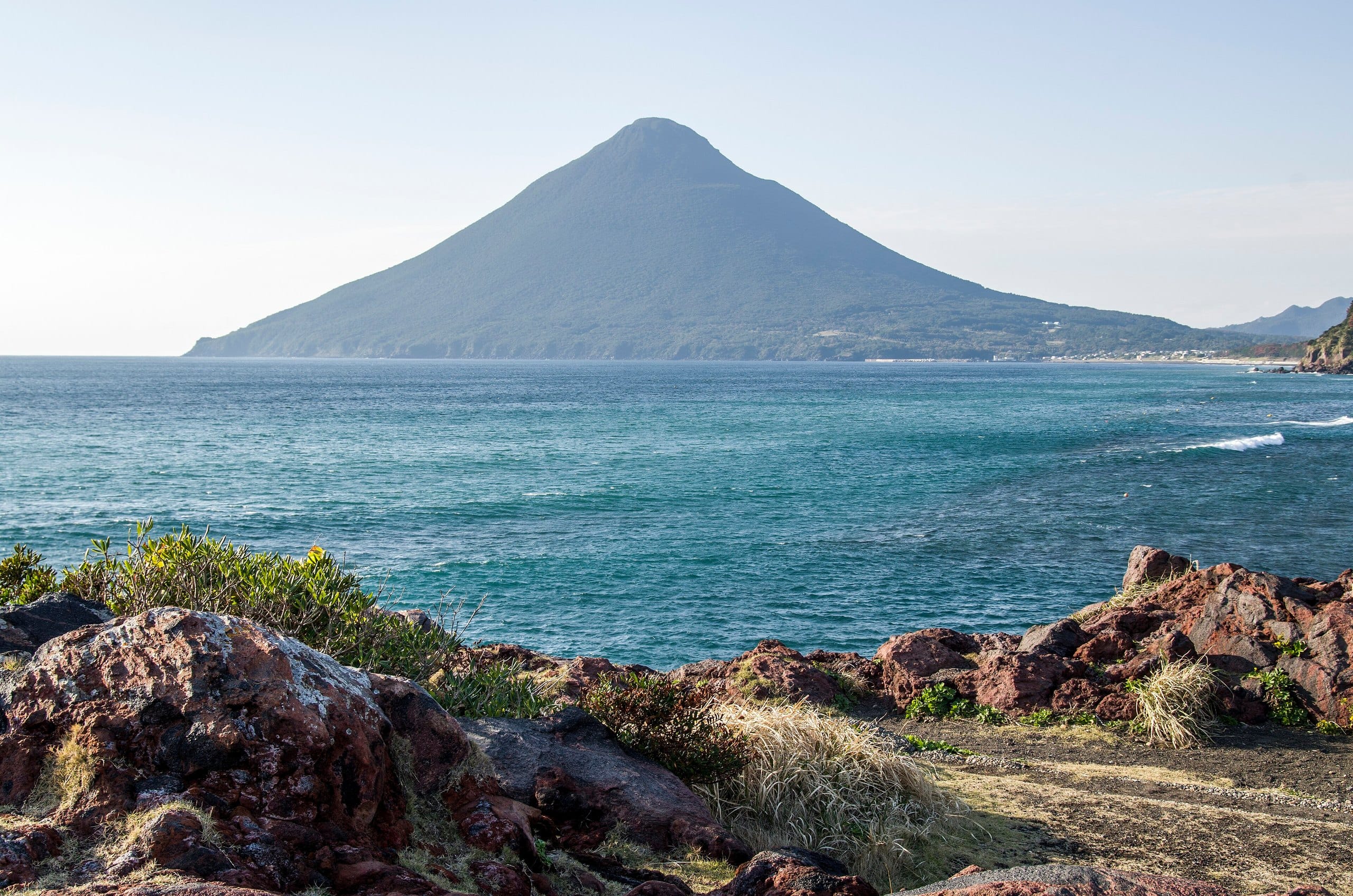 Mount Kaimon rising over blue sea beyond dark volcanic rocks