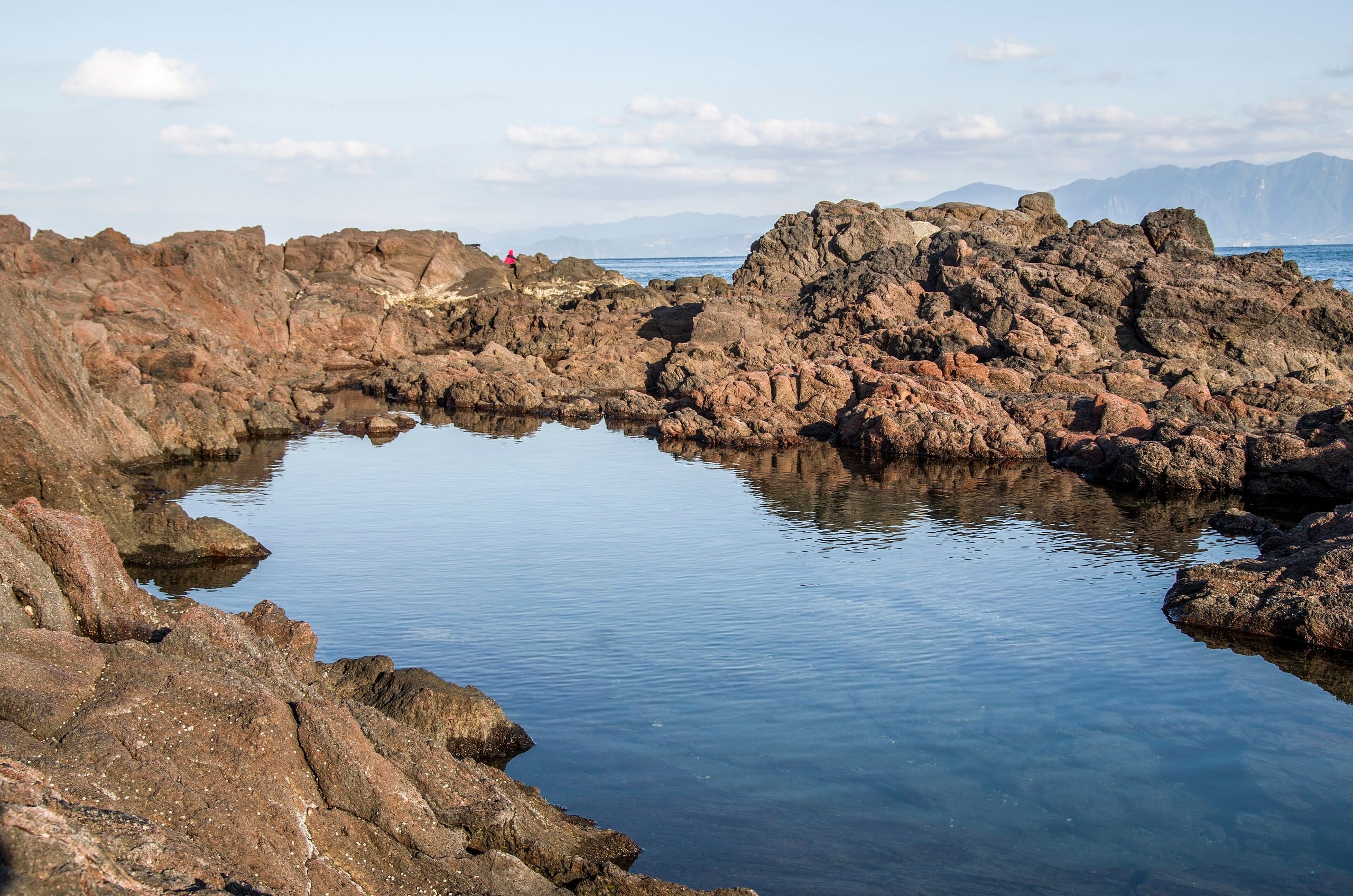 A tidal pool among rugged lava rocks reflecting the sky at Cape Nagasakibana