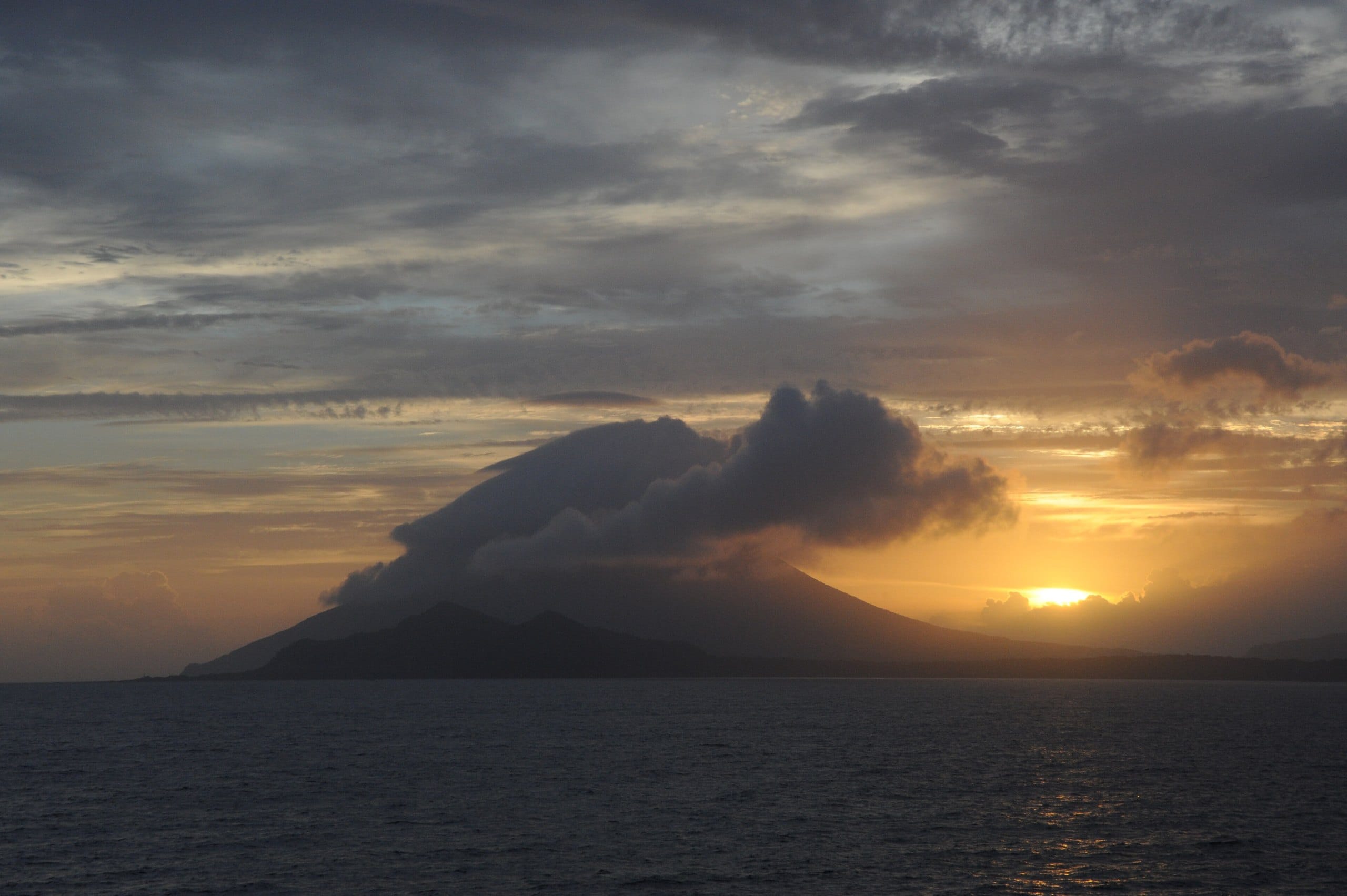 The sun setting behind clouds wrapped around Mount Kaimon over the sea