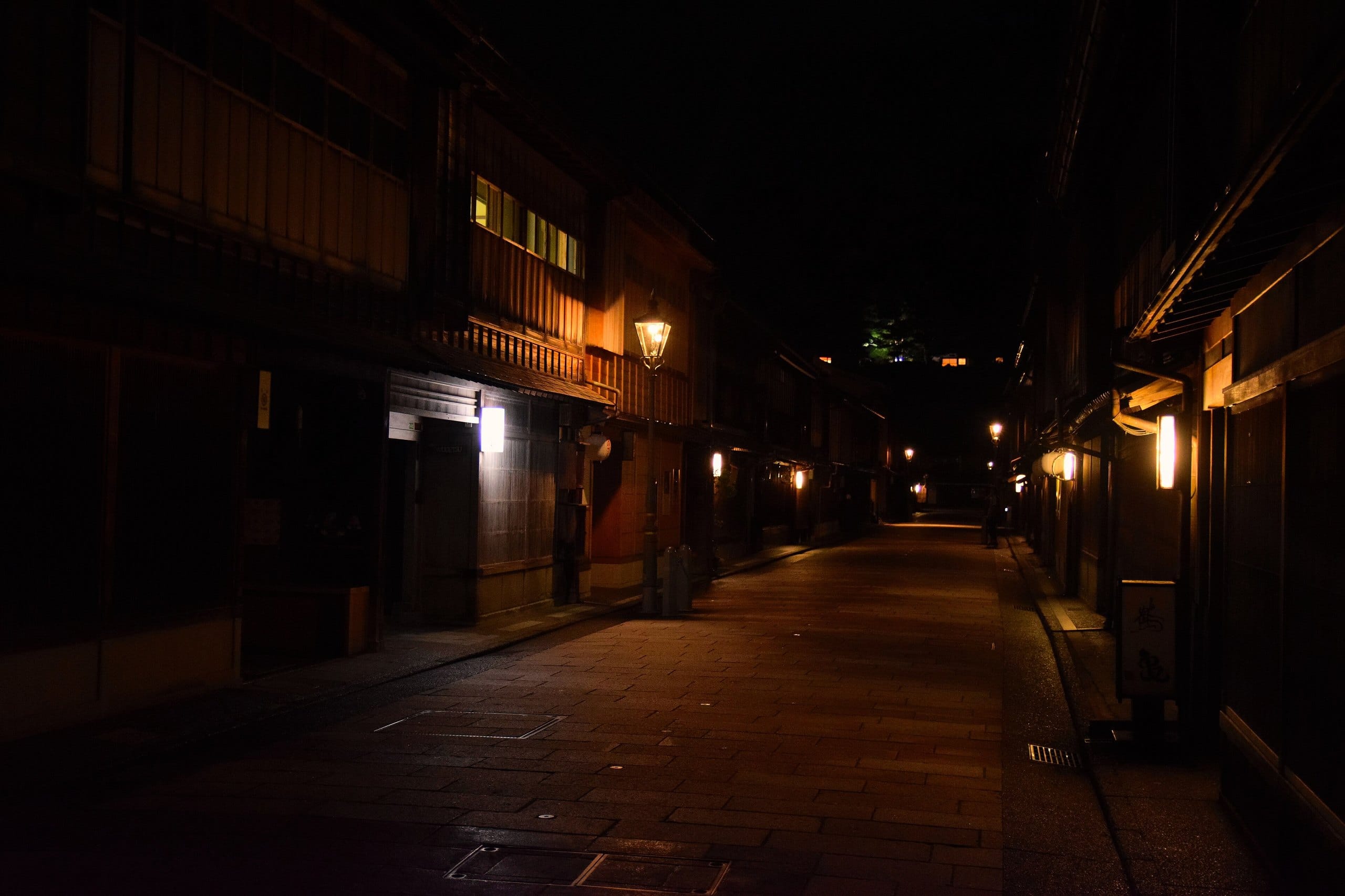 A dark, quiet teahouse lane lit by a single street lamp and warm doorway lights
