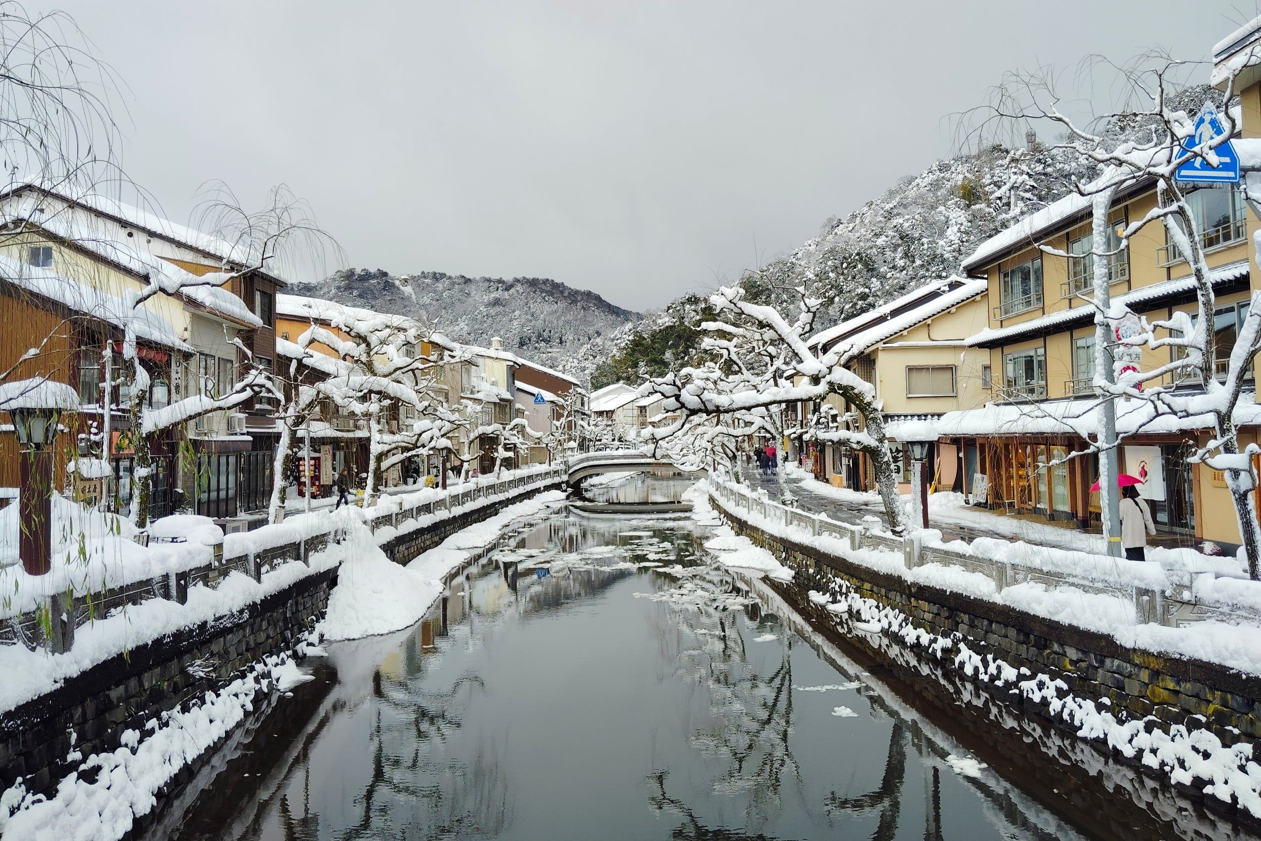 Snow-covered willows and stone bridges along the Otani River in Kinosaki Onsen