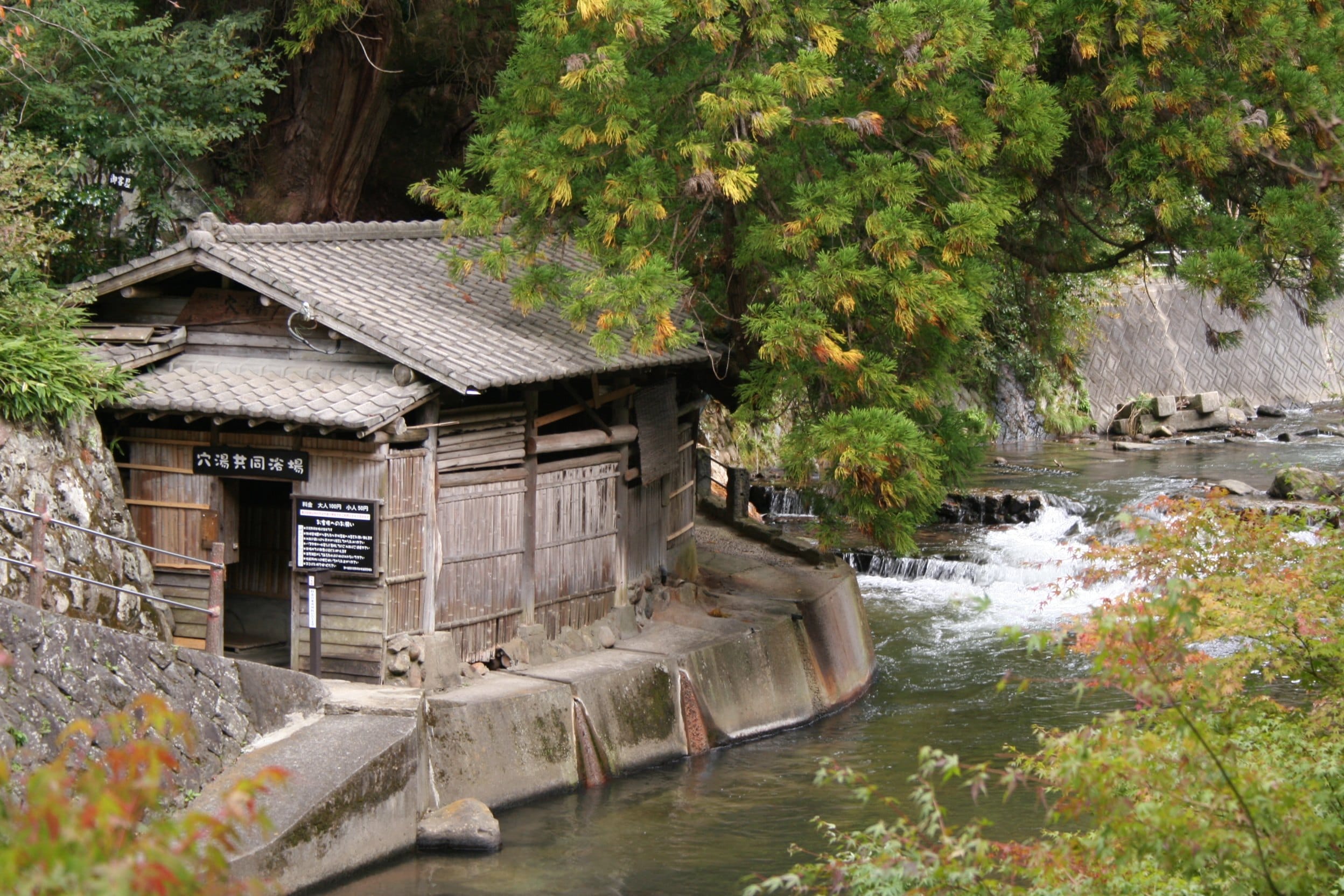 Small wooden communal bathhouse beside the river in Kurokawa Onsen