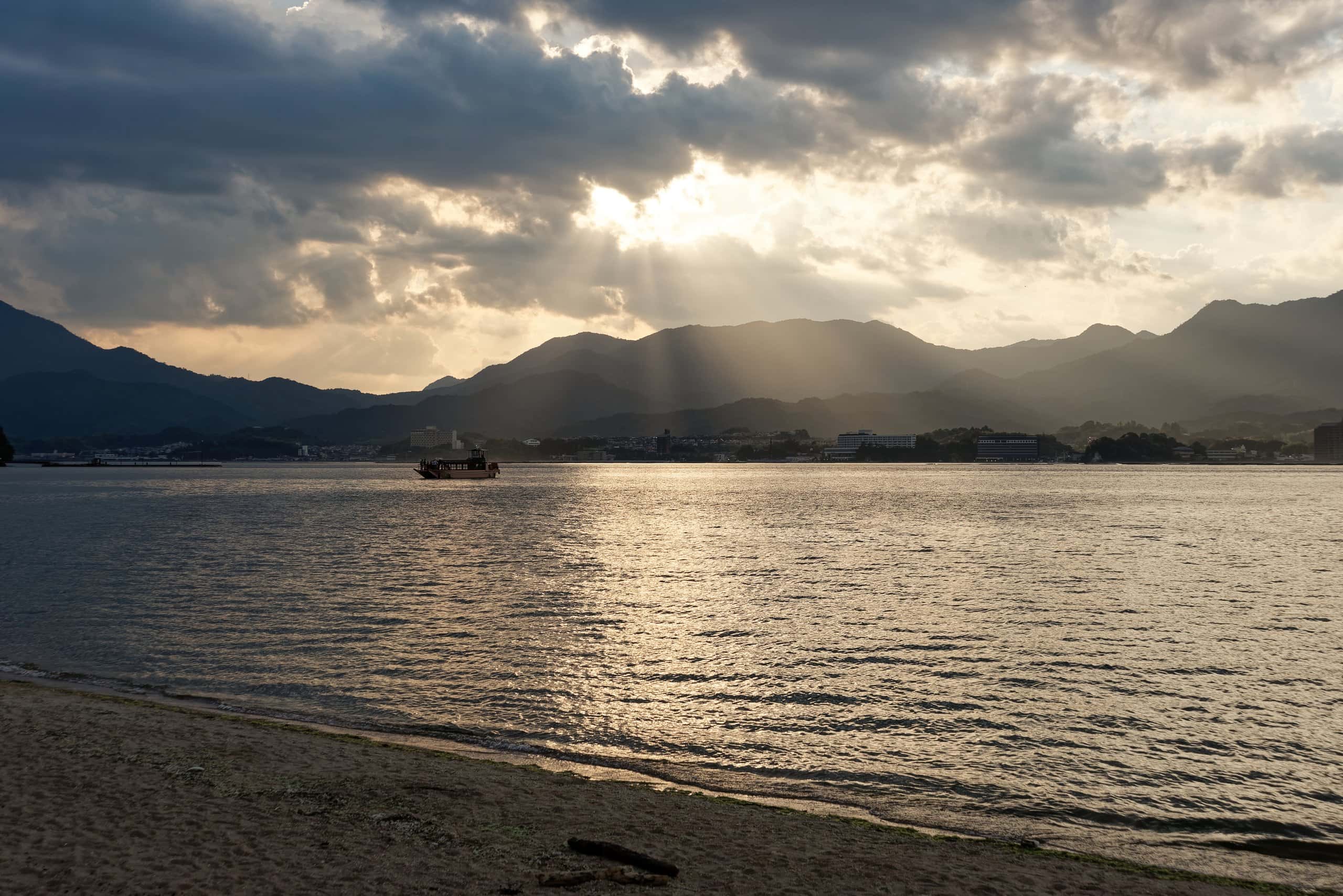 Sun rays breaking through clouds over the calm Seto Inland Sea seen from a Miyajima beach