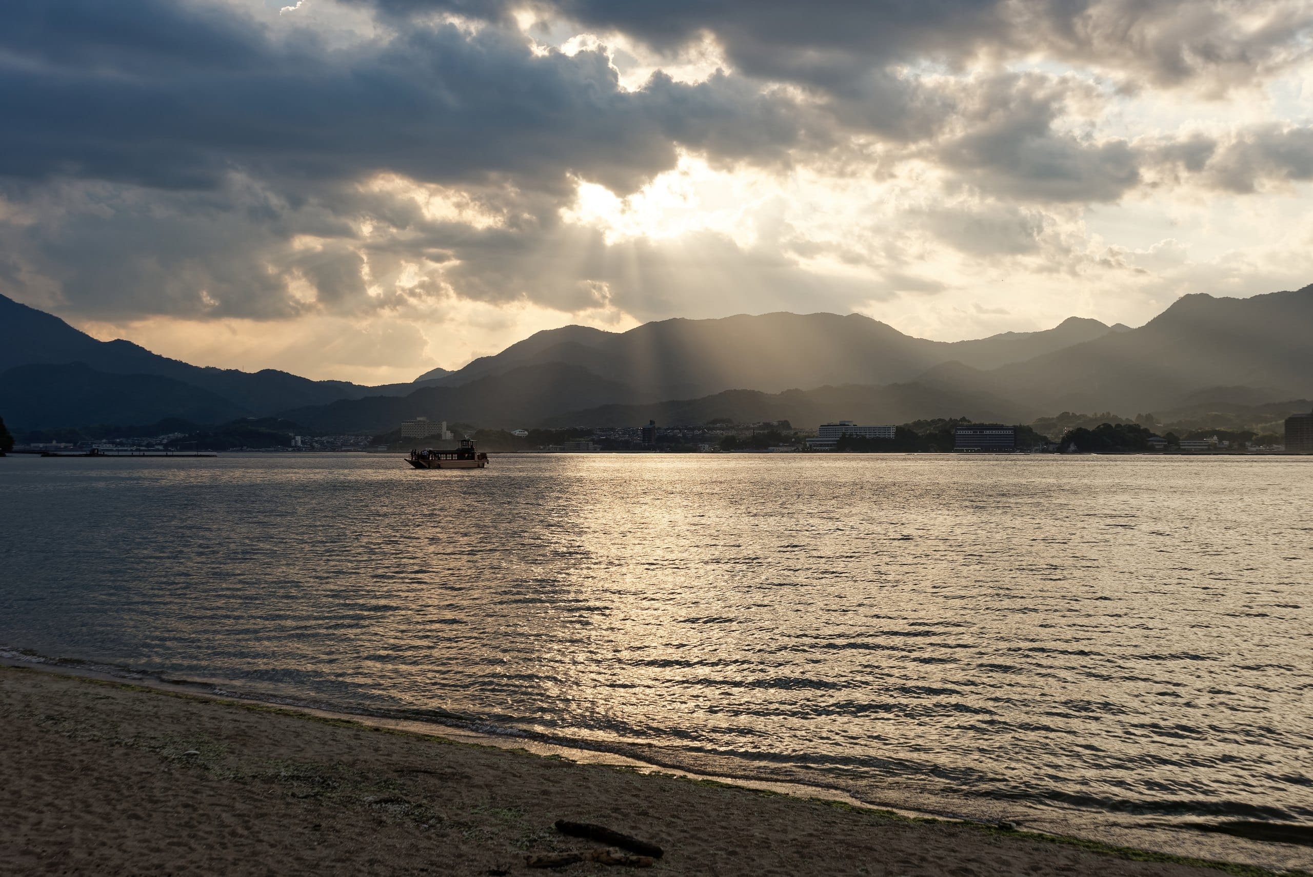 Sun rays breaking through clouds over the calm Seto Inland Sea seen from a Miyajima beach