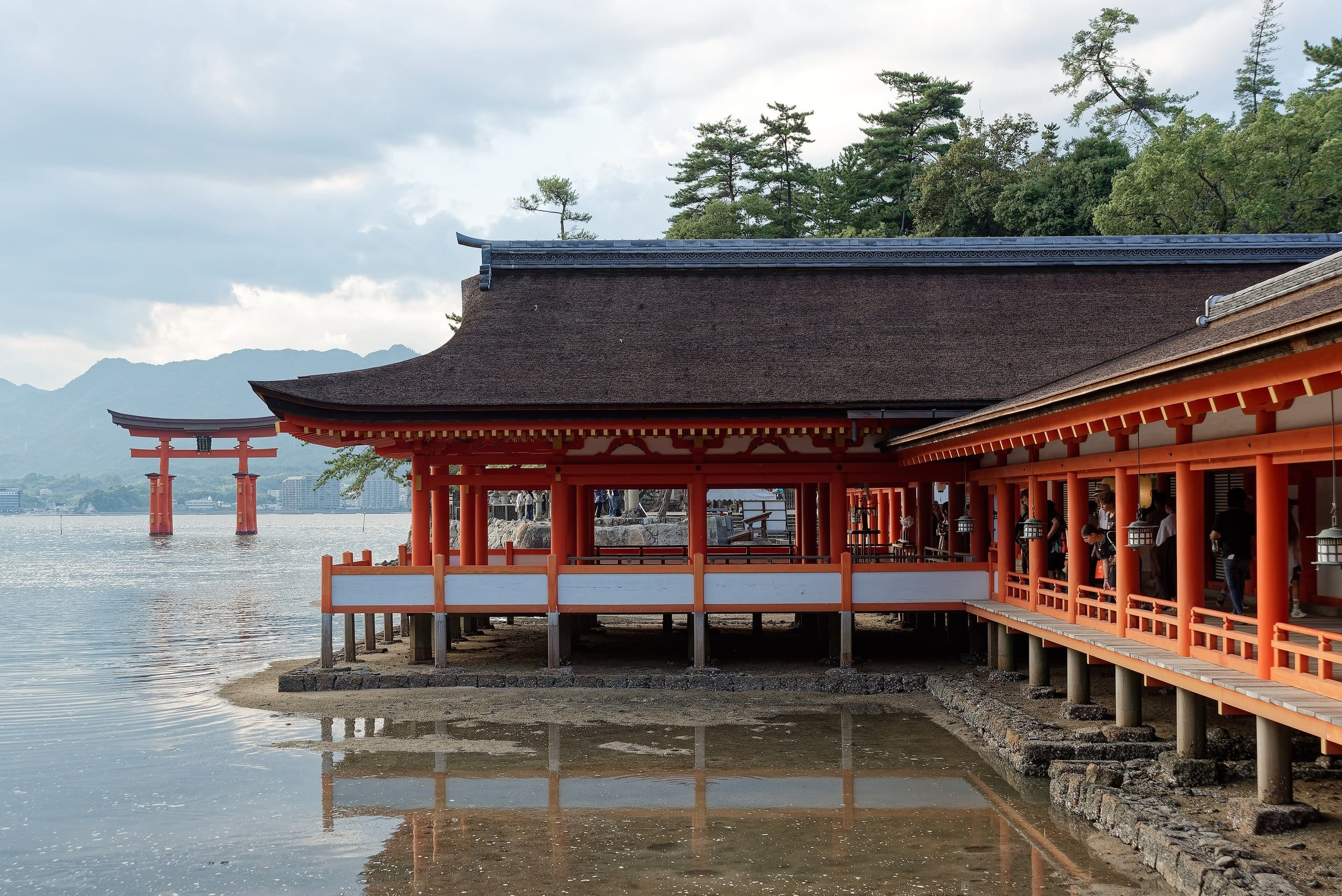 Vermilion shrine corridors standing over tidal water with the floating torii in the distance