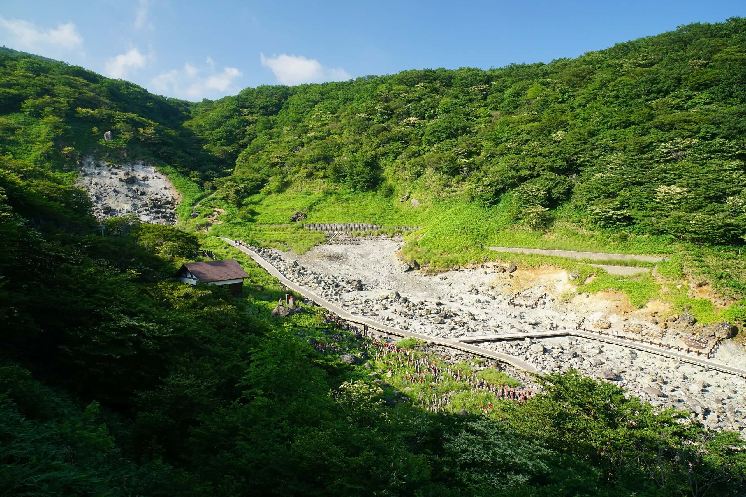 Barren volcanic gully with a boardwalk between green summer hillsides at Sessho-seki