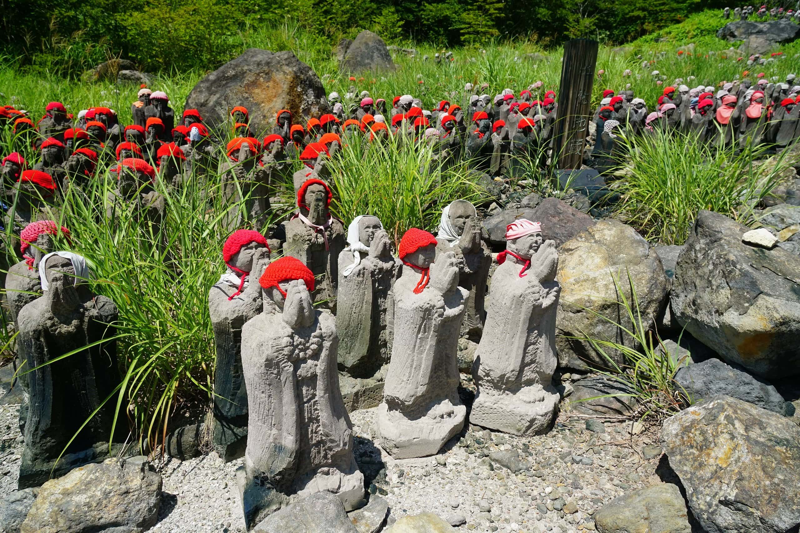 Rows of small stone Jizo statues wearing red knitted caps among rocks