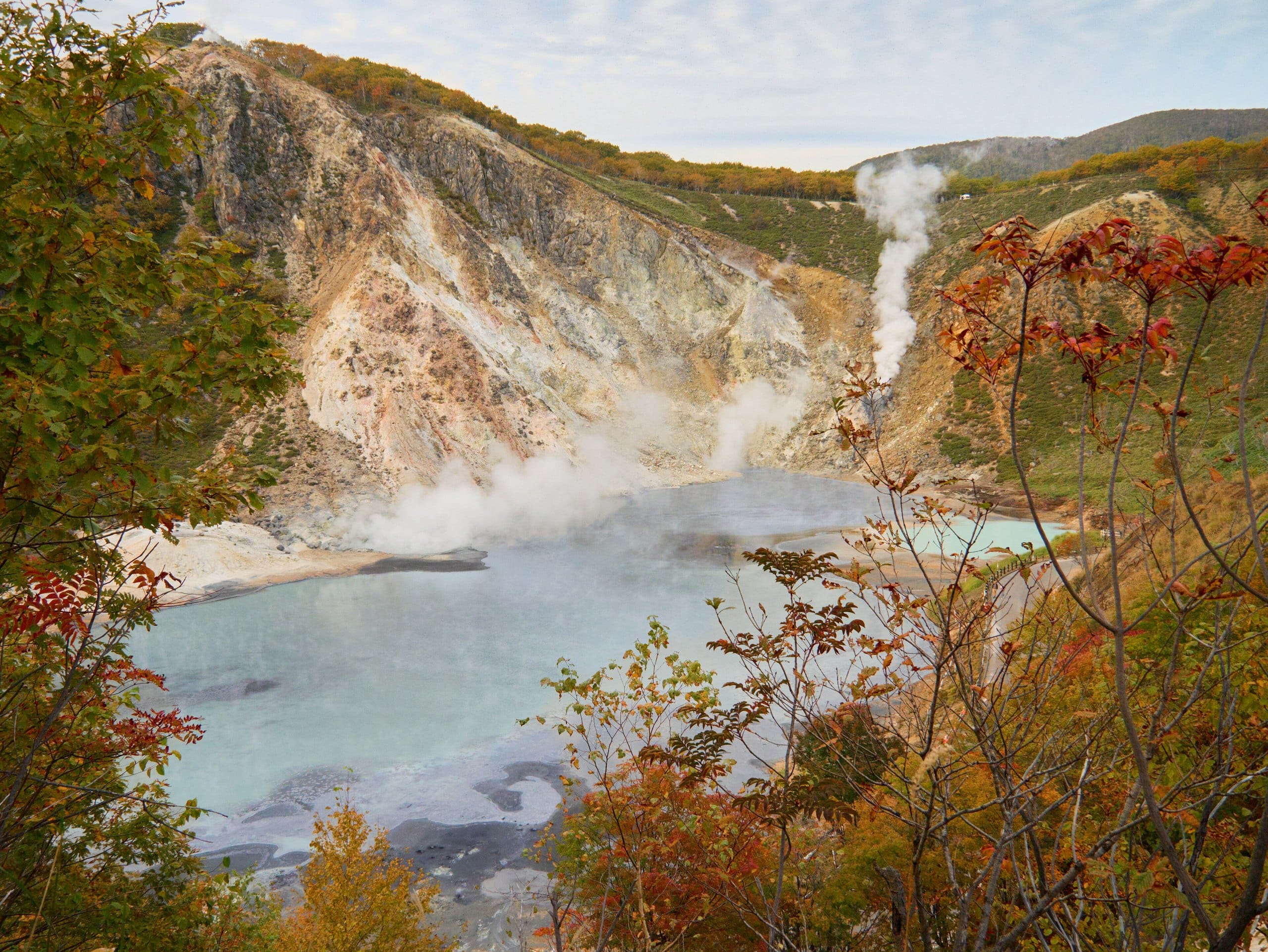 A steaming grey-blue hot spring pond framed by red autumn leaves