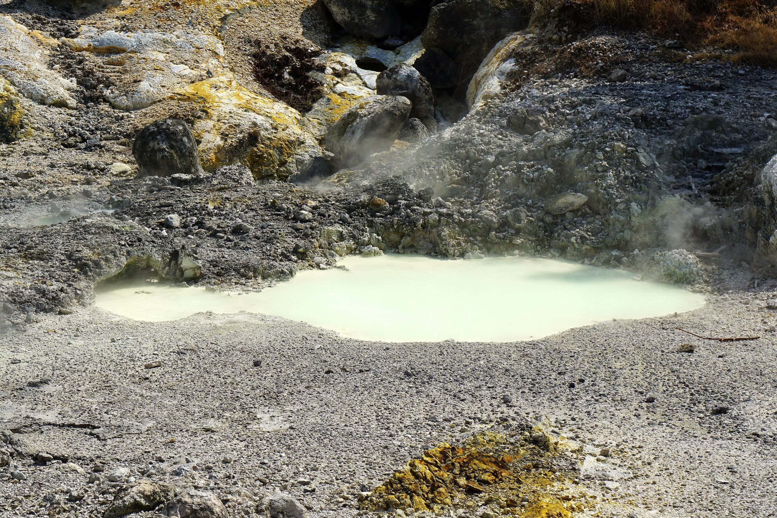 Milky white hot spring pool surrounded by grey volcanic rock