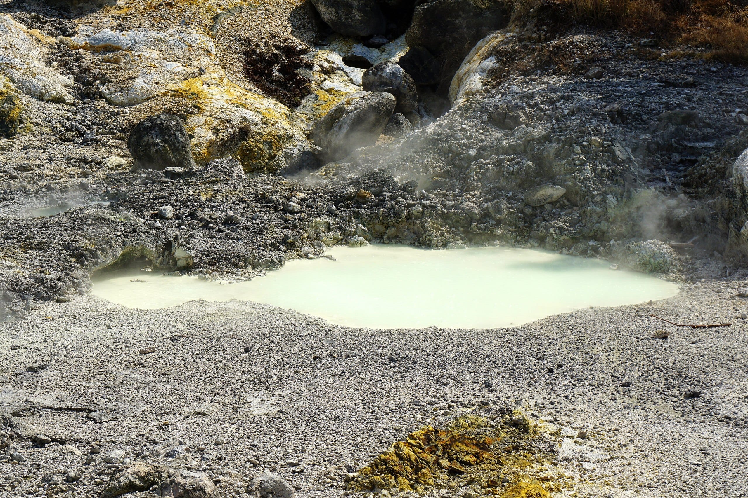 Milky white hot spring pool surrounded by grey volcanic rock