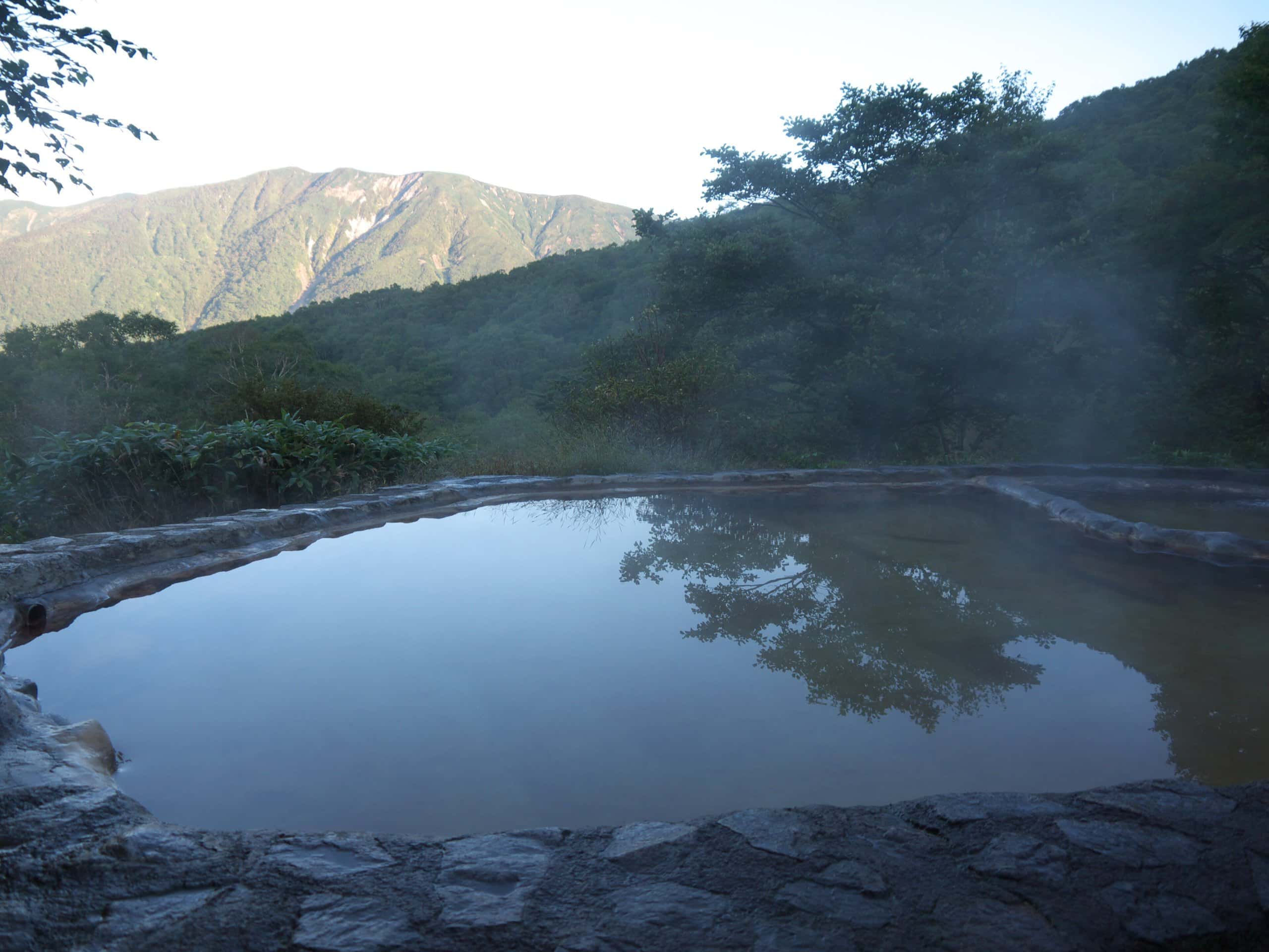 A misty empty outdoor hot-spring pool facing forested mountains