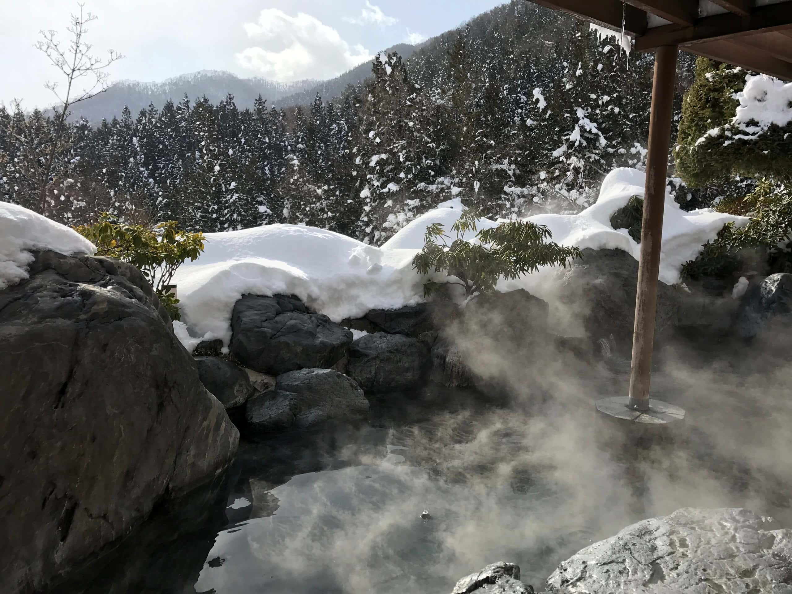 An empty rock-lined open-air bath steaming in the snow