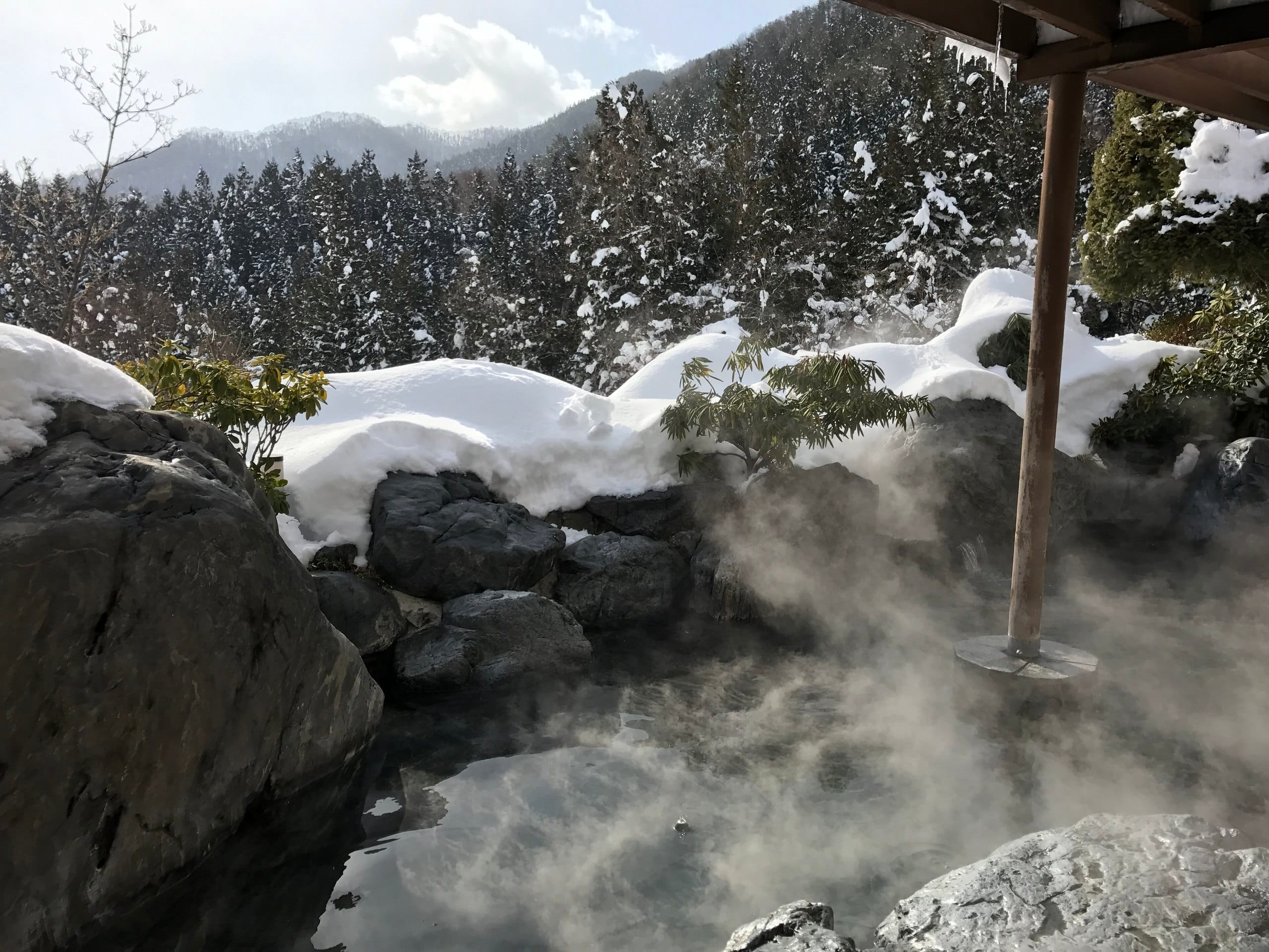 An empty rock-lined open-air bath steaming in the snow