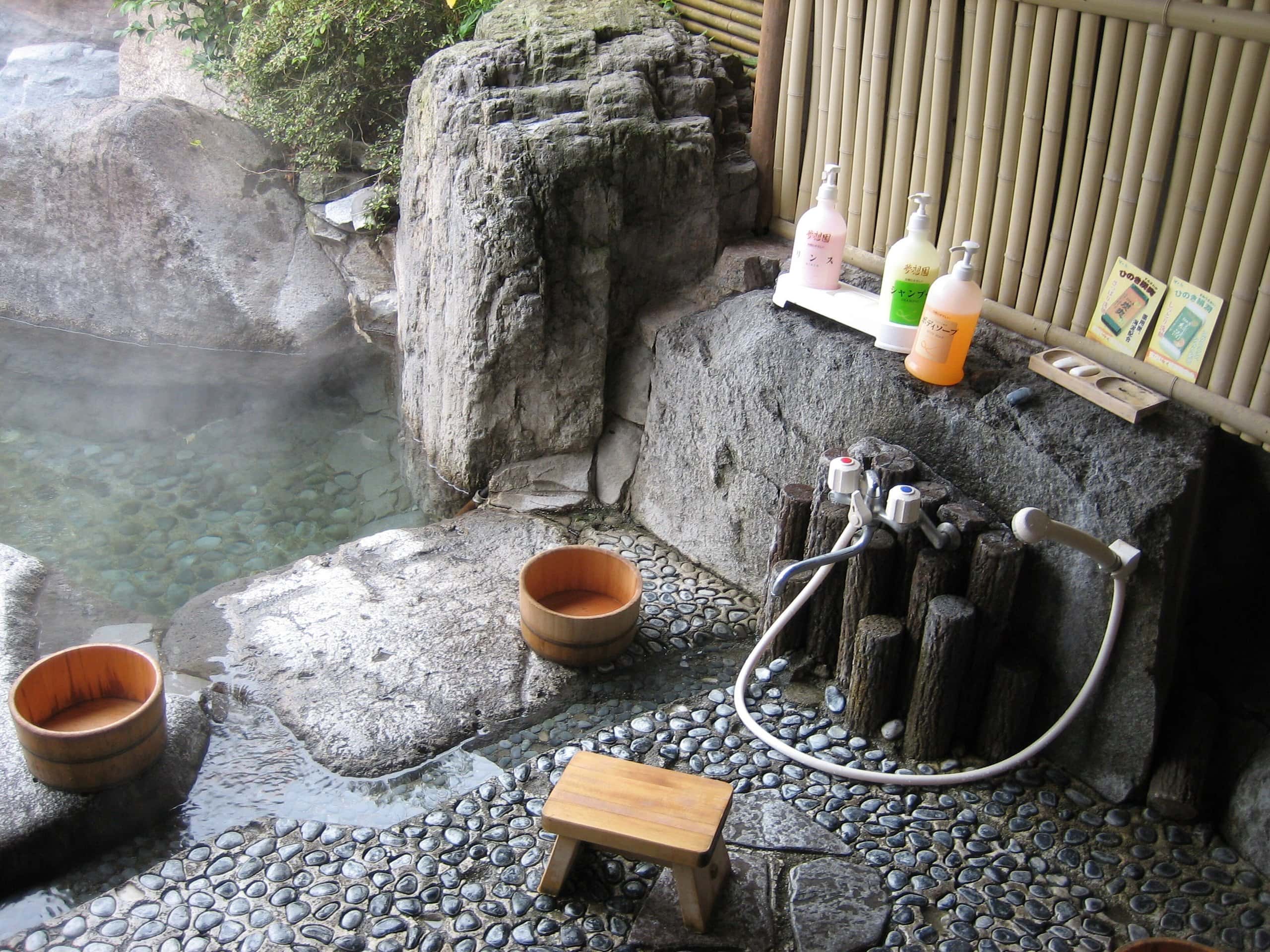 An outdoor washing spot with a wooden stool, pails and a hand shower