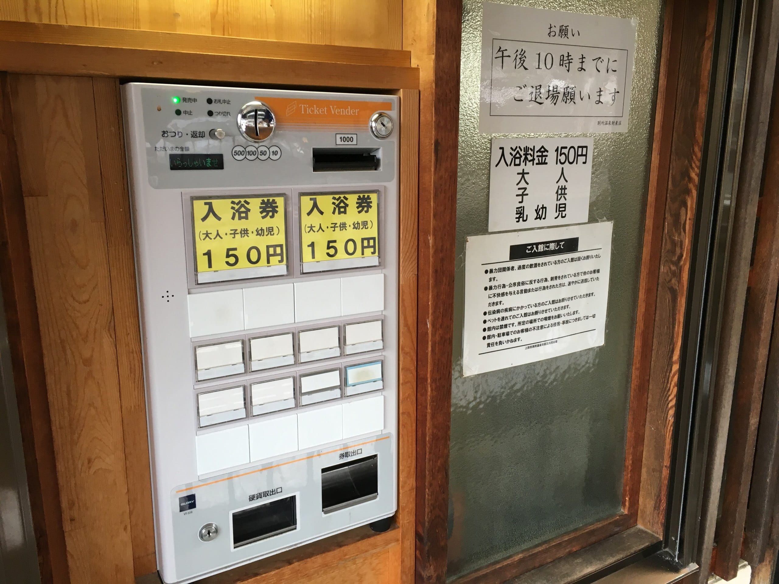A bath-ticket machine beside a printed list of house rules at a day bath