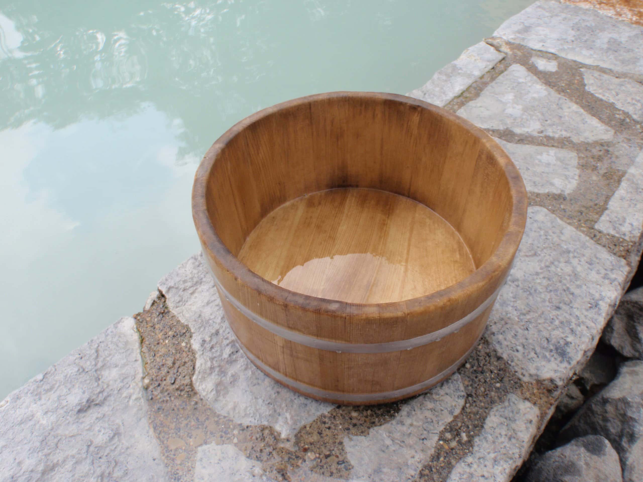 A single wooden bath pail on a stone ledge beside milky hot-spring water