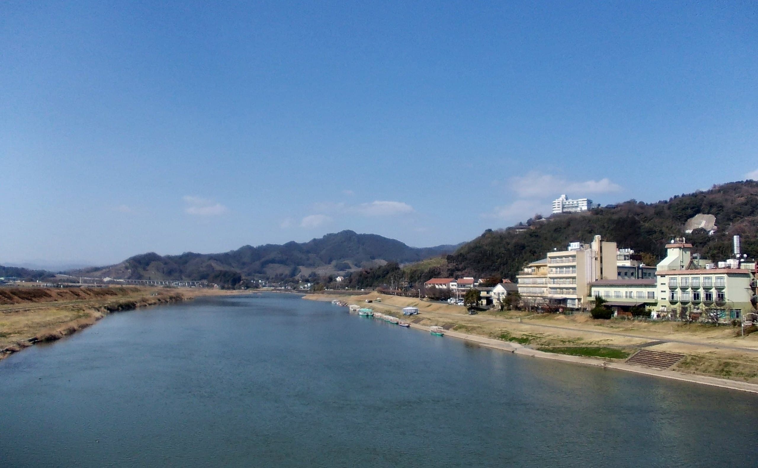 The wide Chikugo River with Harazuru Onsen's buildings on the right bank and low hills behind
