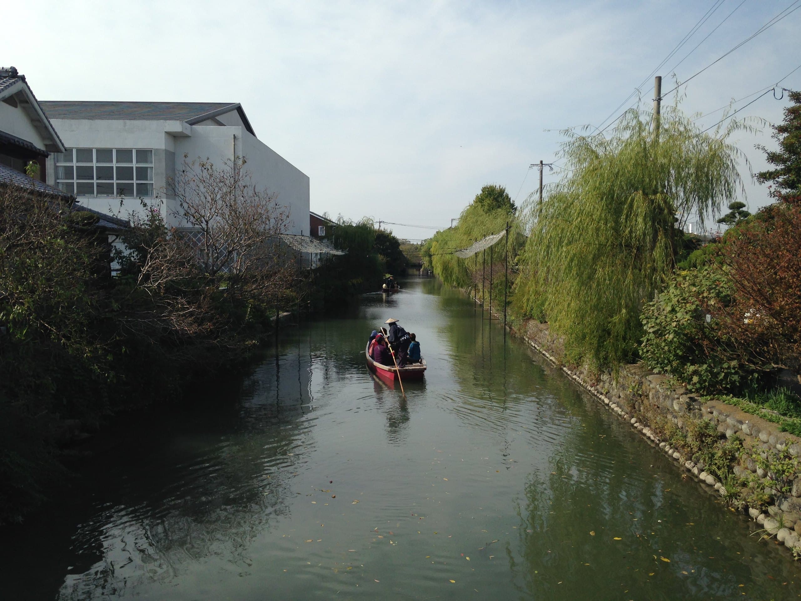 A punt gliding down a canal in Yanagawa, with weeping willows along the stone bank