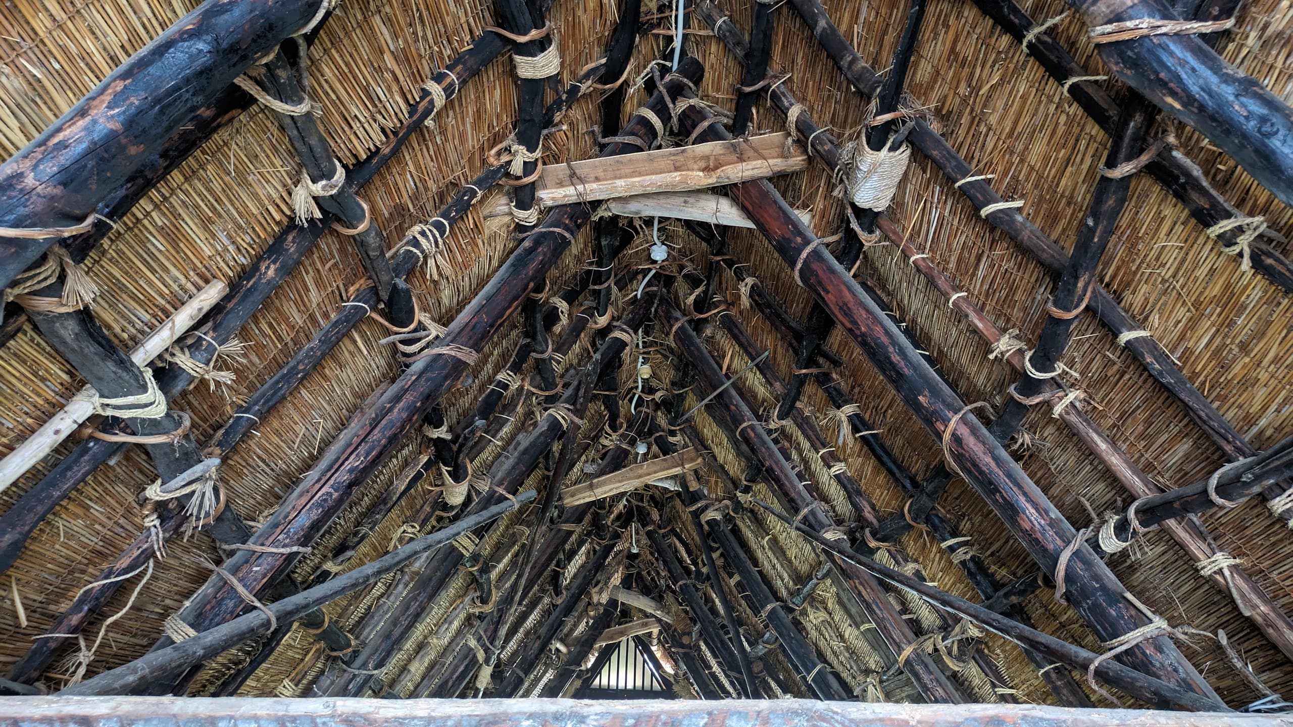 Looking up into a thatched gassho-style roof: bamboo and timber rafters tied with rope